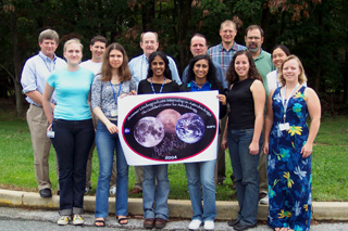 13 people standing outside, displaying a scientific poster