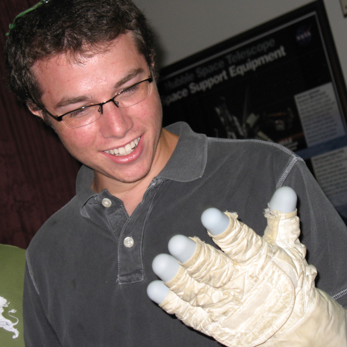 A young man looking at a large white glove on his left hand.